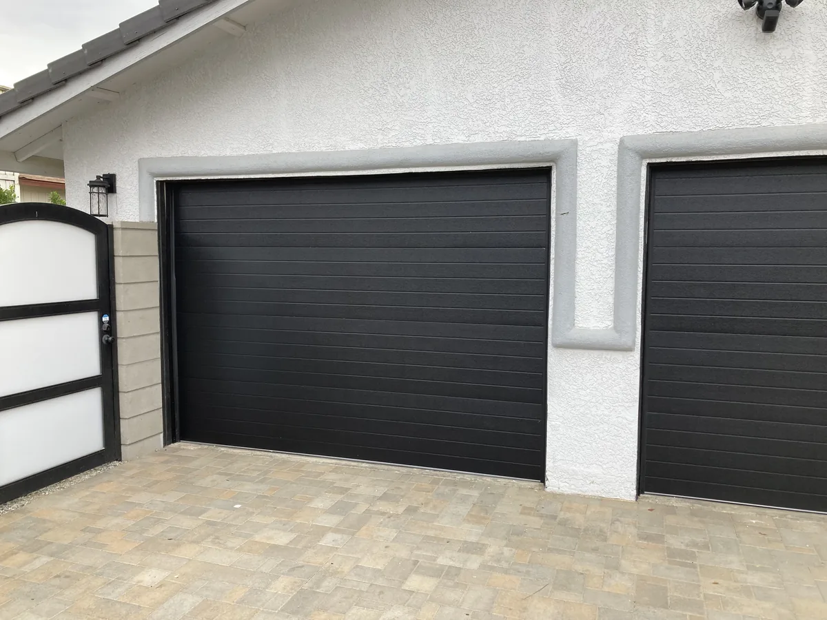 Two black flush panel garage doors on a stucco home