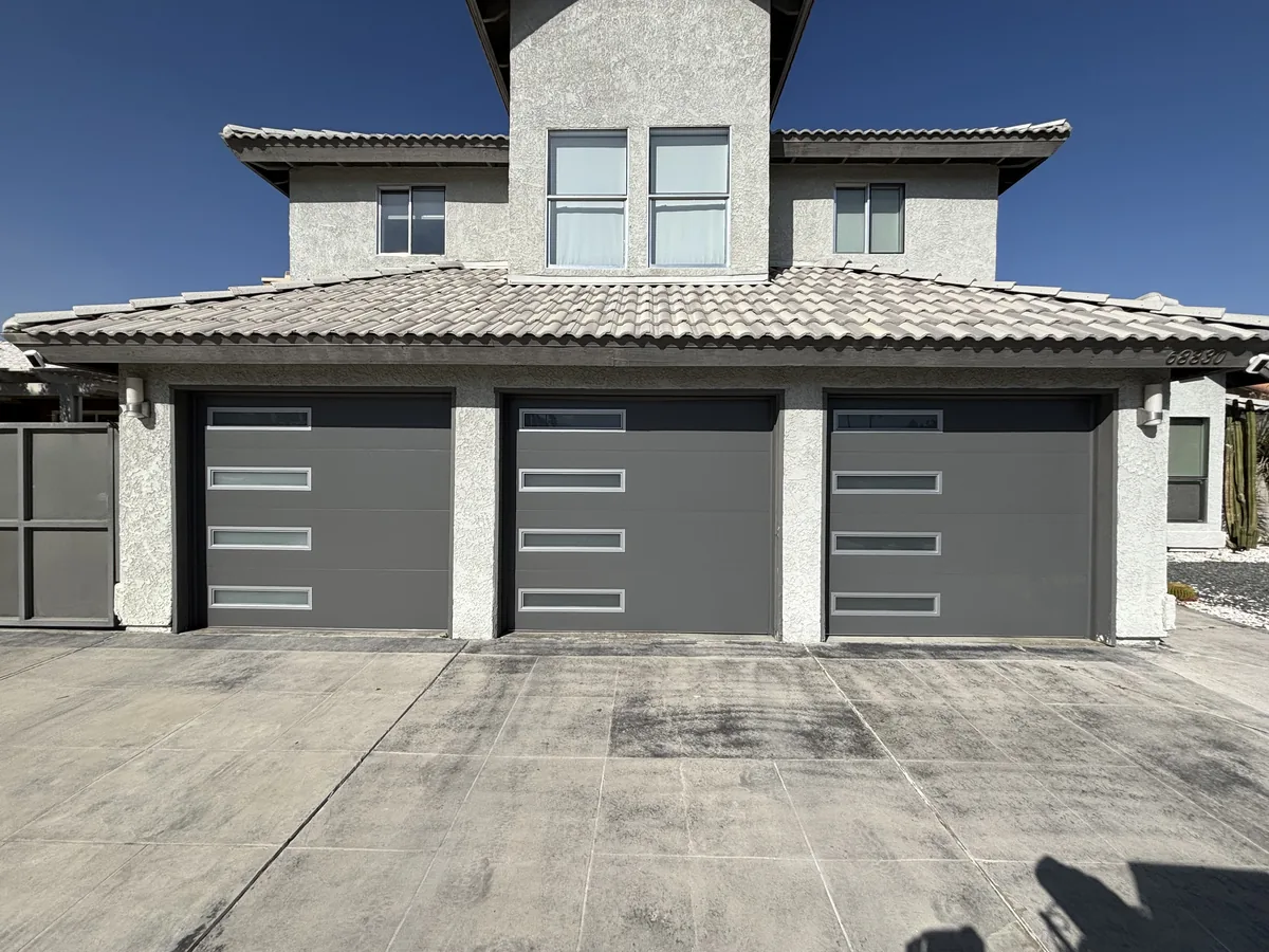 Three dark modern garage doors with vertical window slots on a two story home